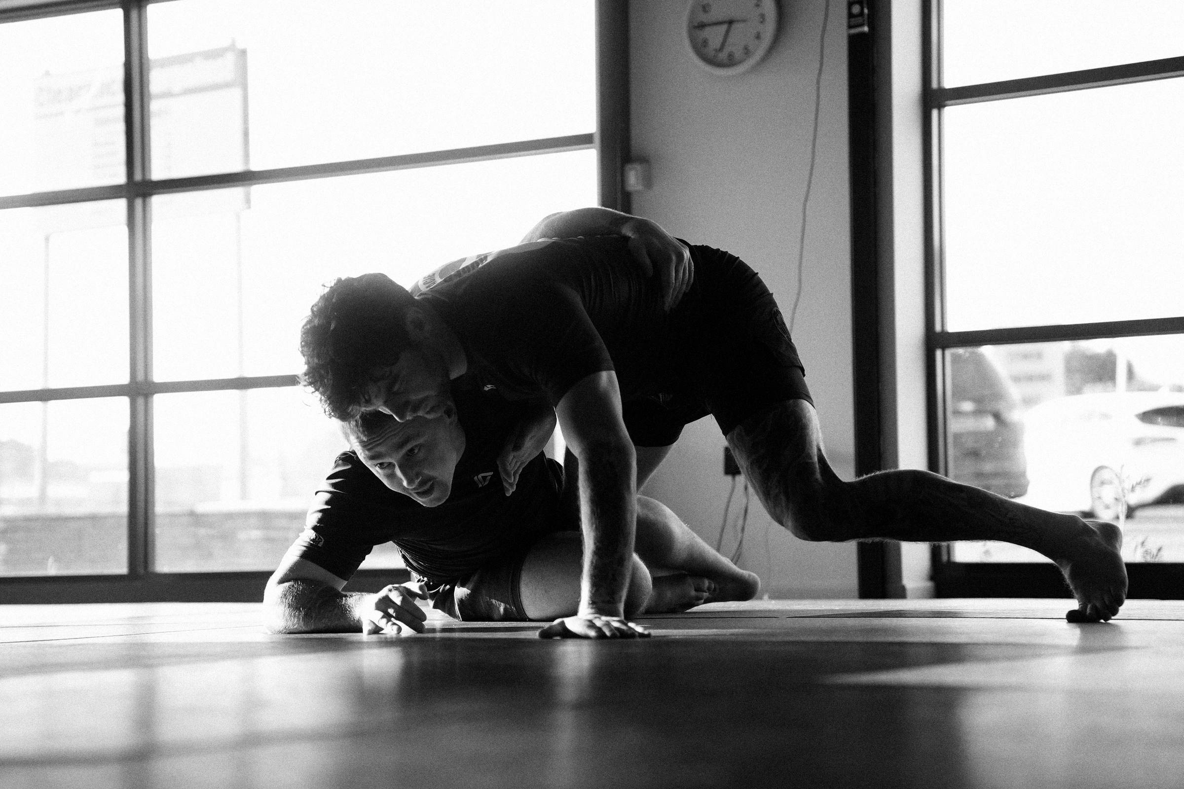 Two members training no-gi by the academy windows